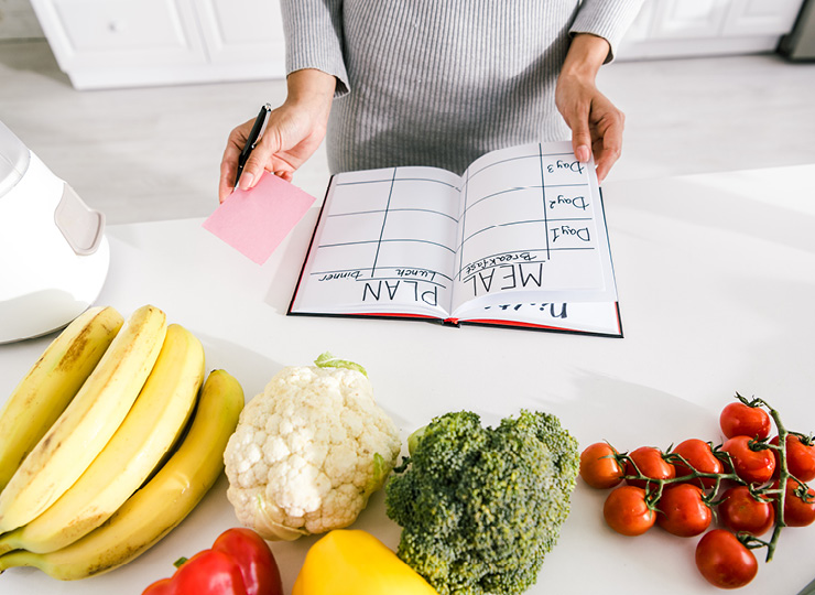 Person writing their meal plan in a diary, Fruits and vegetables on the table